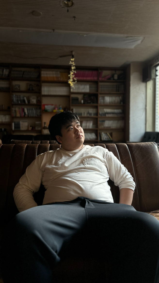本棚のある部屋でソファに座る顔面土砂崩れ
